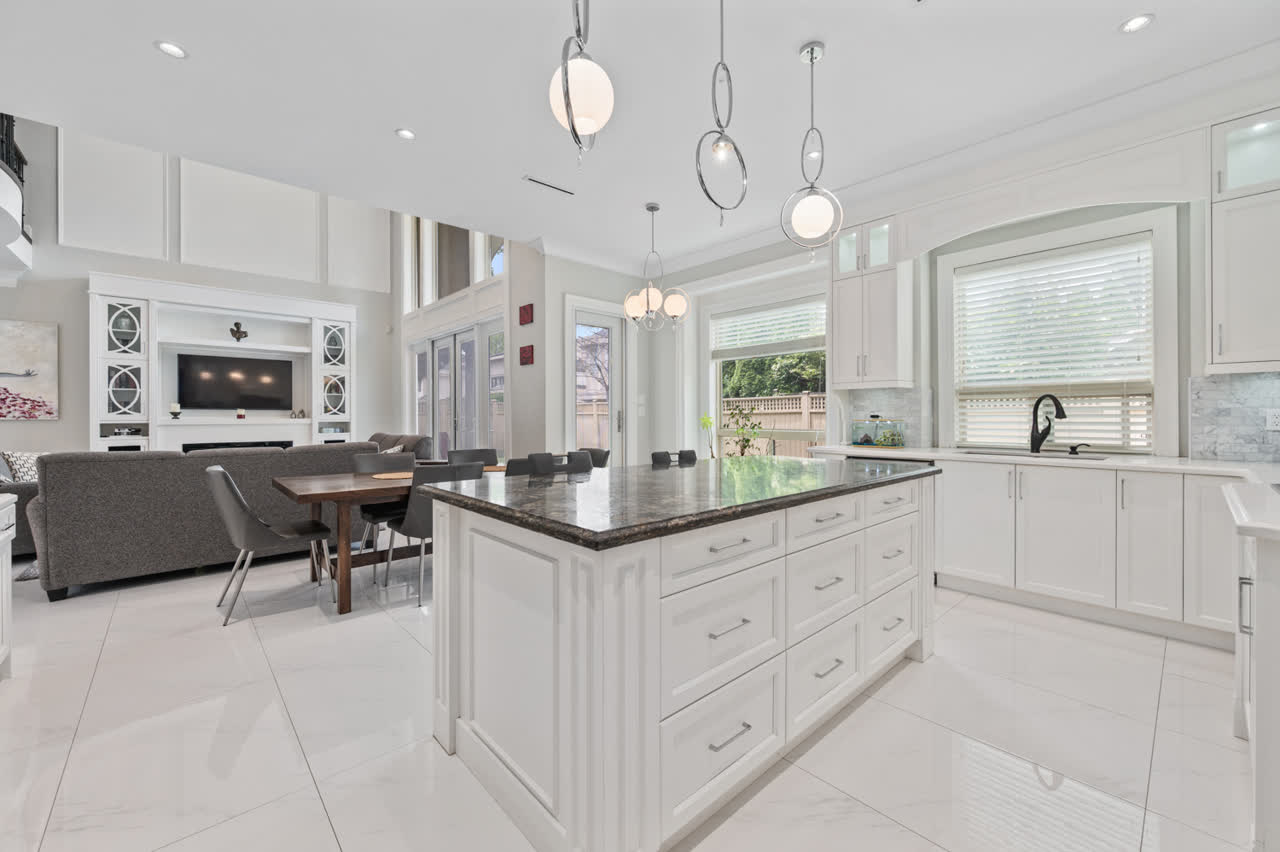 Open-plan white kitchen with a dark granite island, glass pendant lighting and a living area beyond