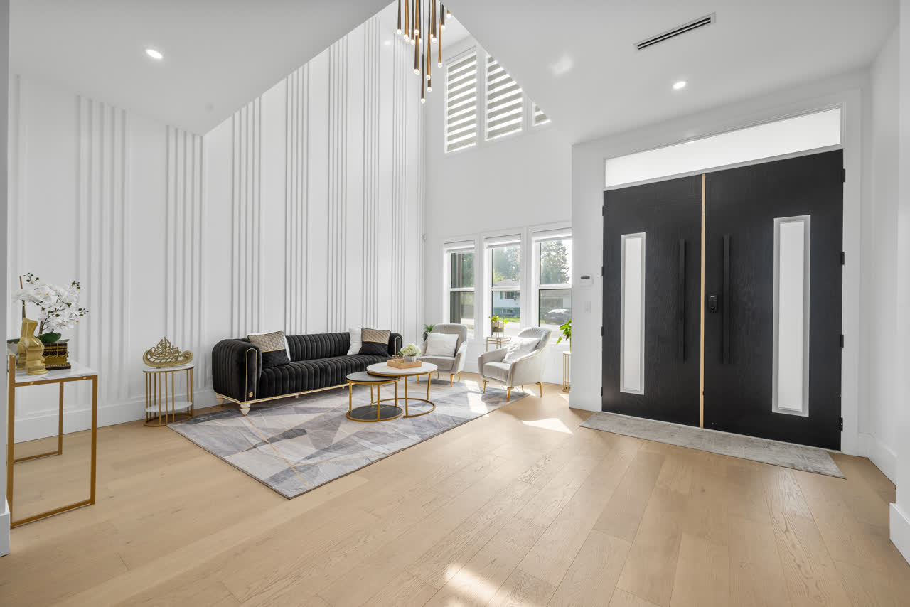 Double-height entry hall with pale oak floors, tall black double doors and a fluted white feature wall