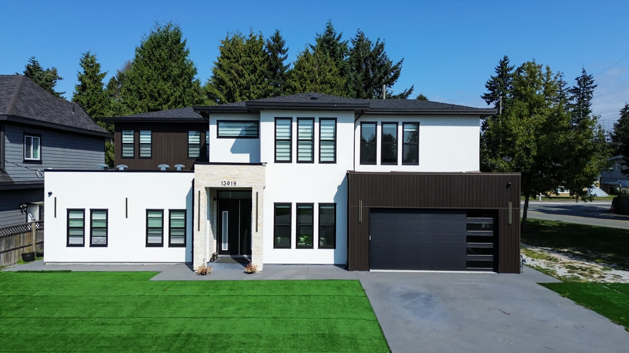 Modern white and black two-storey home photographed from above, with a manicured front lawn and double garage
