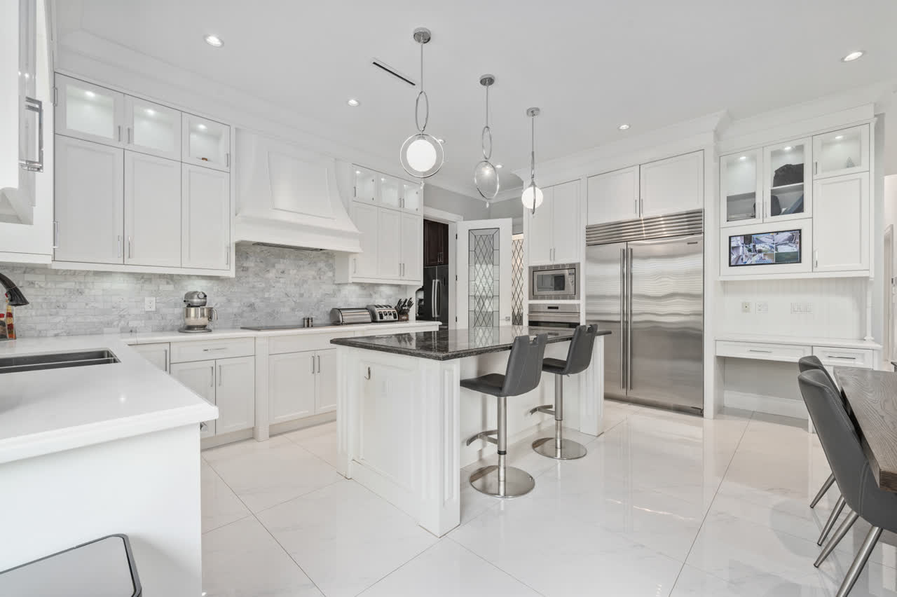 White shaker kitchen with a marble tile backsplash, stainless steel appliances and bar seating at the island