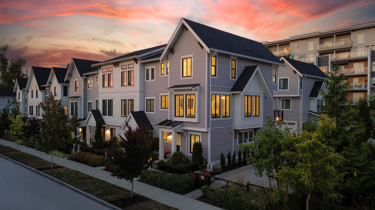 Row of three-storey townhomes at twilight, warm interior lighting glowing against a pink sunset sky